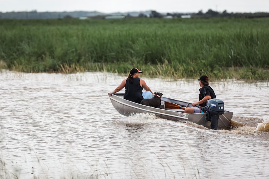 A pair drive a tinnie along a flooded section of a highway.