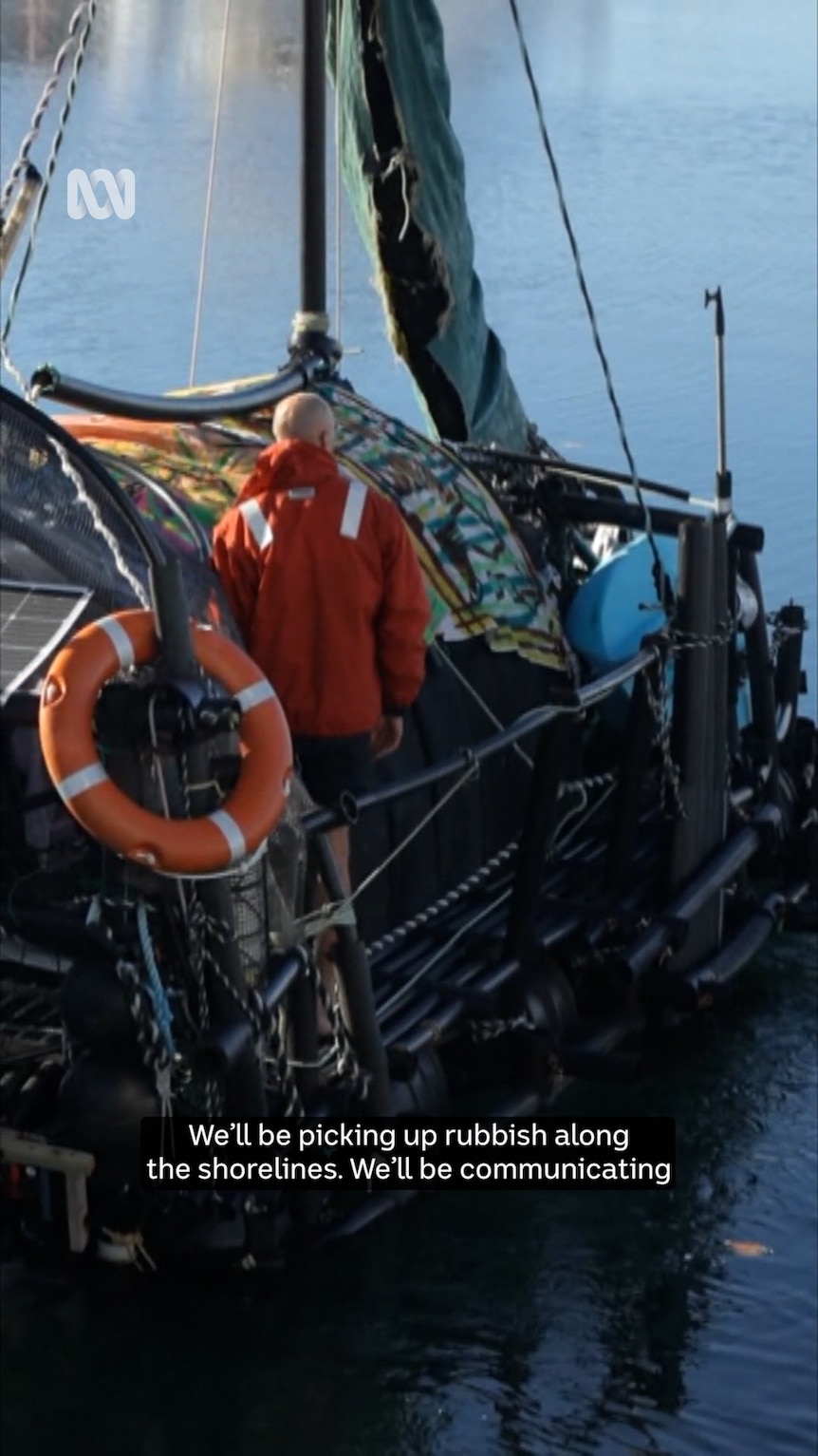 A boat on the water is shown from behind in a tight frame. A person in an orange jacket and a life ring can be seen on board.