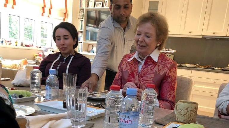 Princess Latifa sits at a table with Mary Robinson. There are bottles of water on the table, a man clears a plate between them