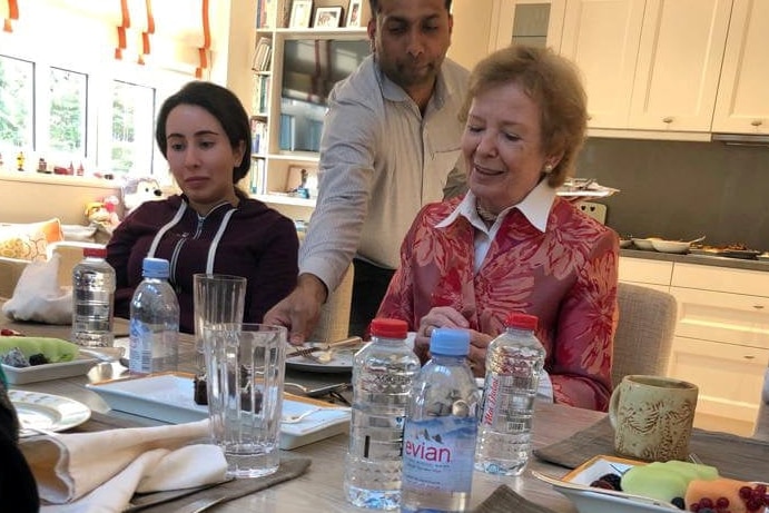 Princess Latifa sits at a table with Mary Robinson. There are bottles of water on the table, a man clears a plate between them