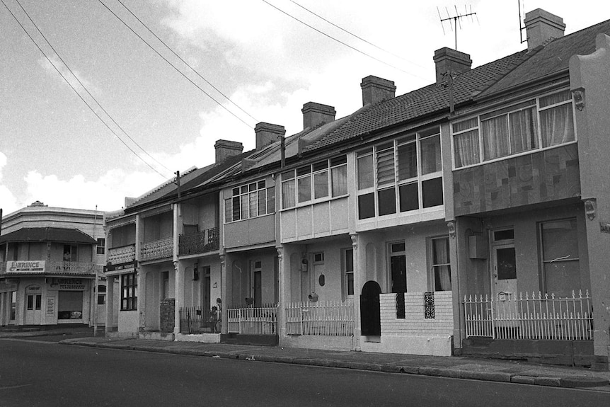A black and white photos shows a row of Victorian row houses on a bare street in Sydney on an overcast day.