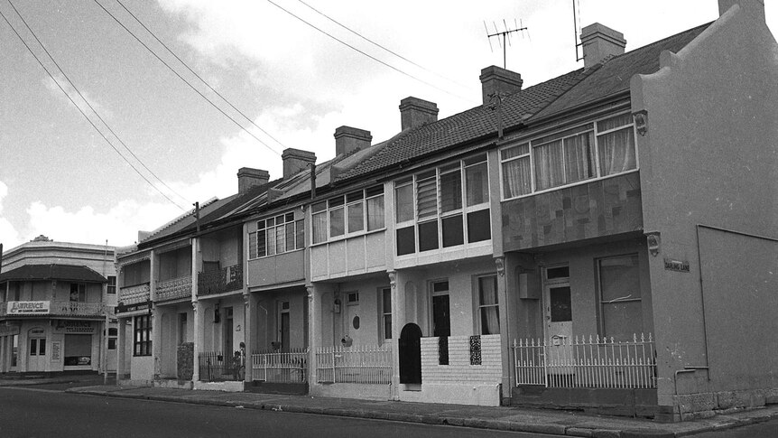 A black and white photos shows a row of Victorian row houses on a bare street in Sydney on an overcast day.