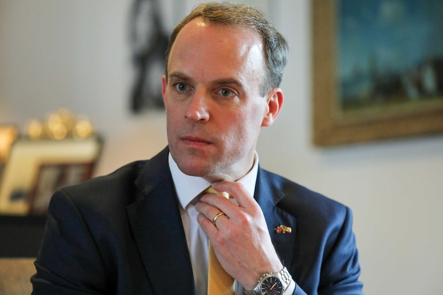 Dominic Raab looking serious, adjusting his tie