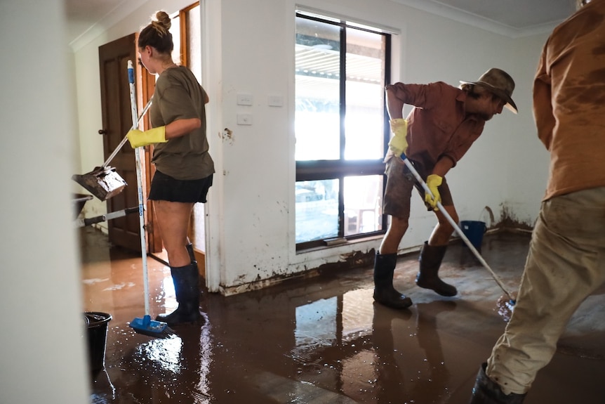 Two people clean mud from the floor inside a house
