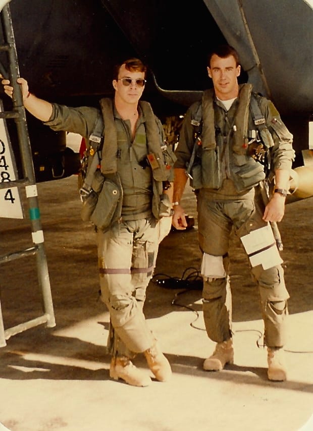 Two US Air Force men lean against an open fighter jet ready to board.