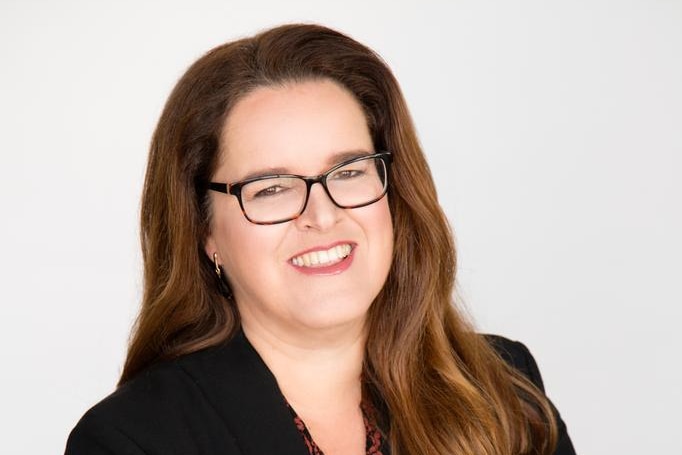 A corporate profile shot of Danielle Mazza, smiling and wearing a black blazer with her arms crossed