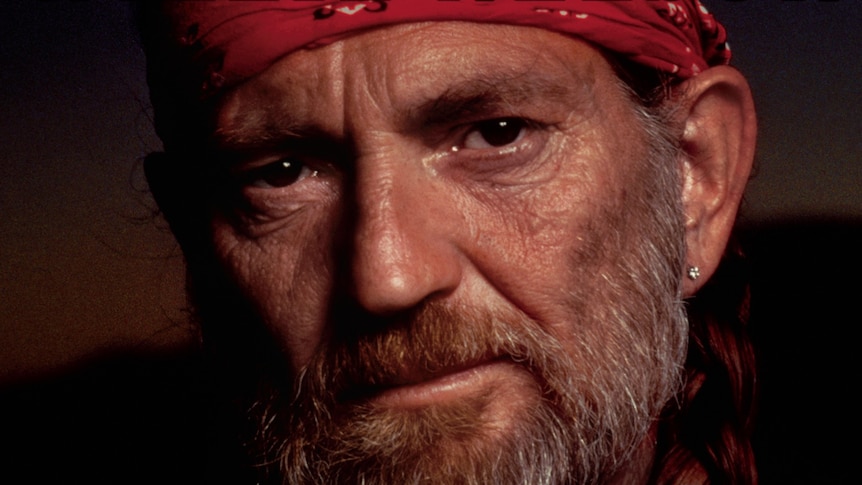 a bearded willie nelson looks sternly at the camera. he has an earring in his left ear.