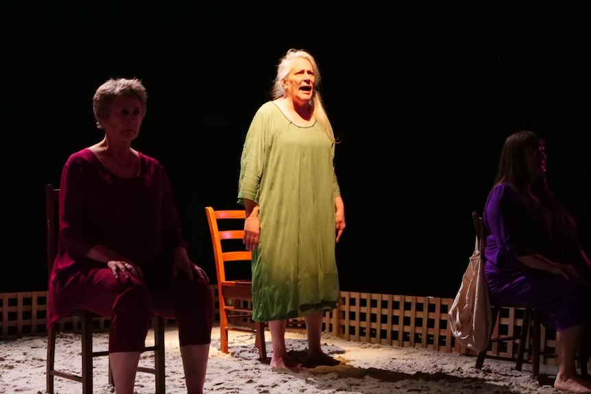 An actor in a green dress is lit by a spotlight as she performs on stage.