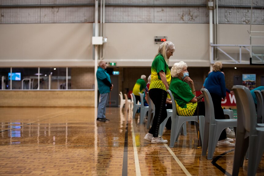 Older people in a large gymnasium, half full.