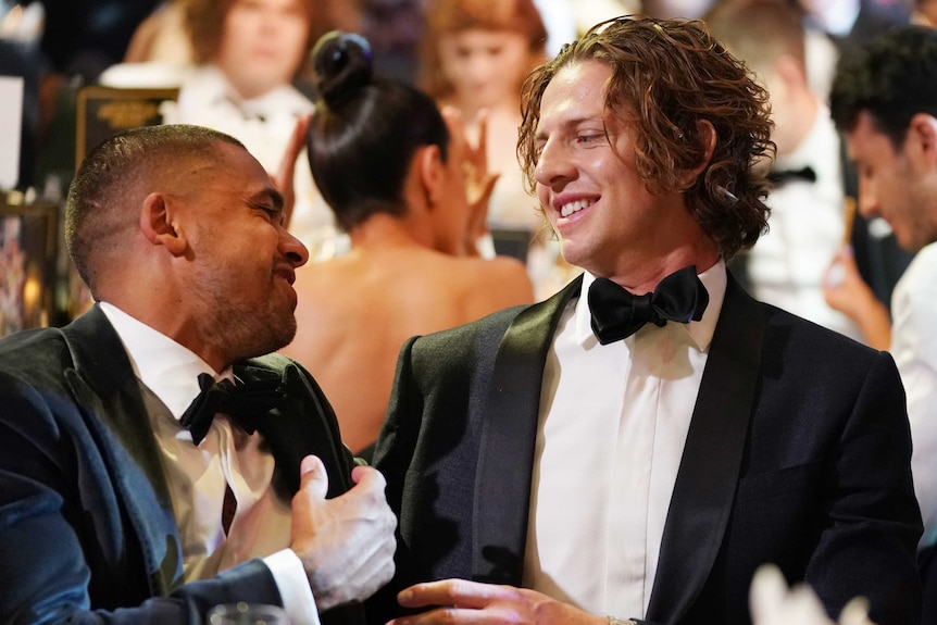 Nat Fyfe and Brad Hill smile while sitting at a table with suits on.