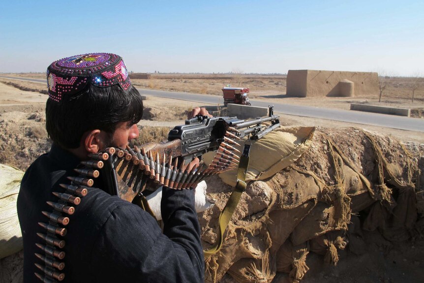 An Afghan police officer with a gun keeps watch during an ongoing battle with Taliban militants.