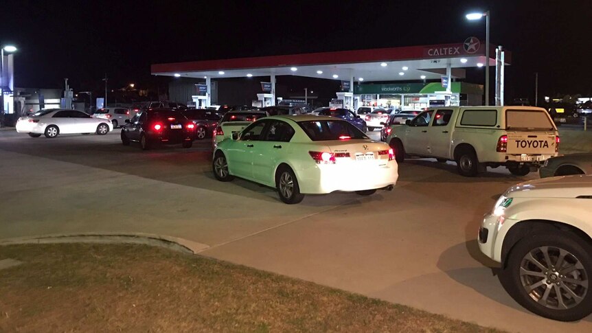 Cars queued up at night on a petrol station forecourt.