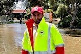 A man wearing a hi-vis vest and a hat standing in front of flooded road