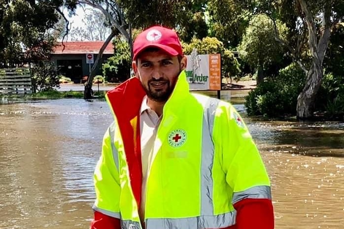 A man wearing a hi-vis vest and a hat standing in front of flooded road