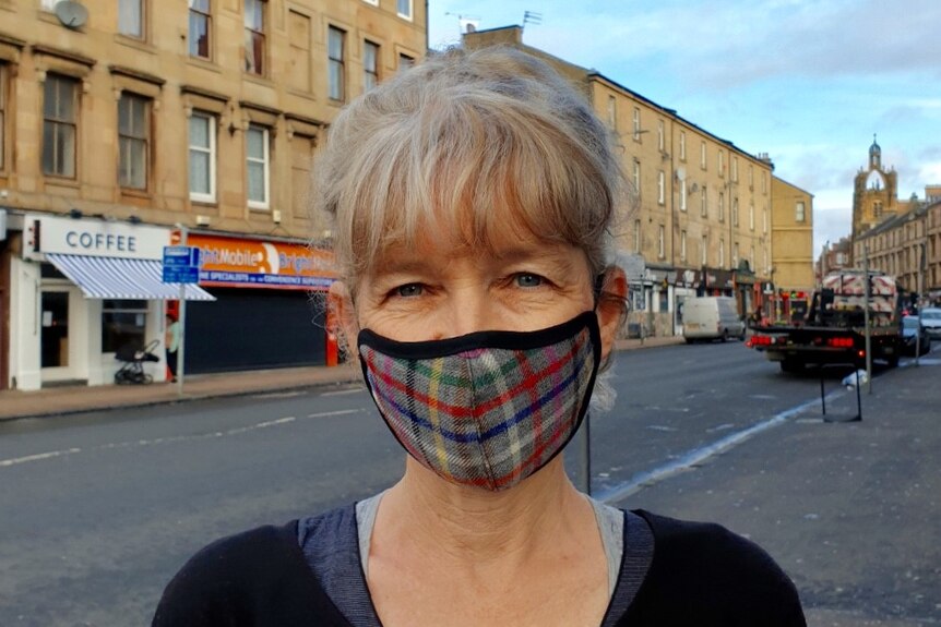 woman stands in street with tartan mask on
