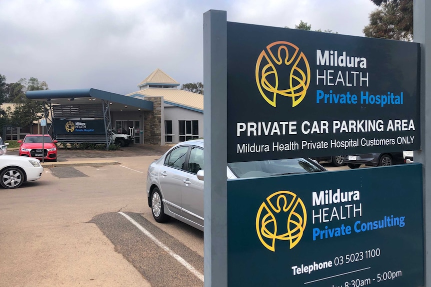 A sign featuring the Mildura Health Private Hospital logo in front of a car park and a building.