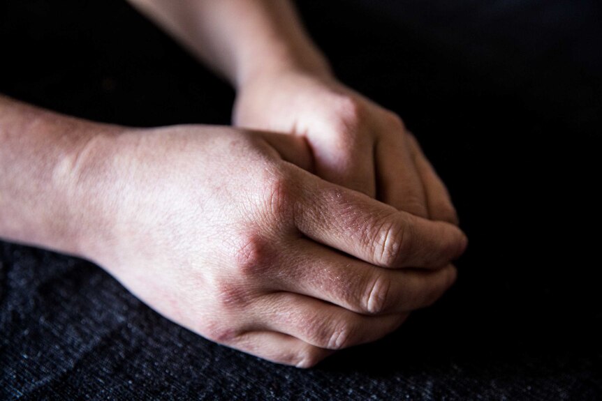 A person's hands sit in their lap, one folded over the other.
