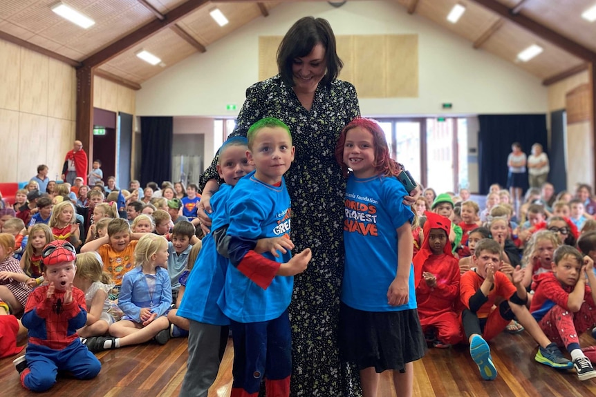 A mother and her three children with shaved and coloured hair standing in front of a hall full of children in superhero costumes