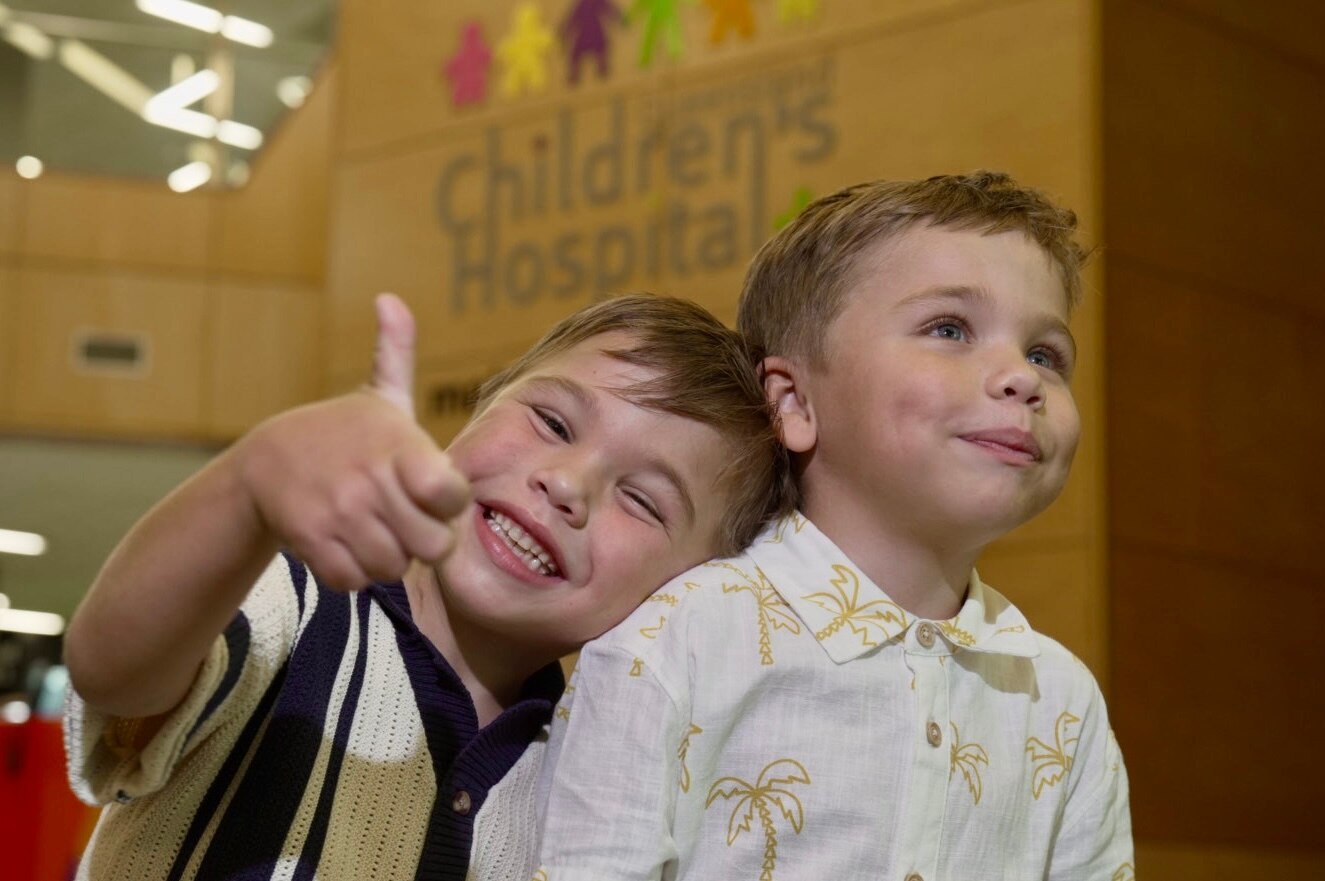 Twin boys Louis and Theo are smiling and leaning on each other during a visit to hospital.