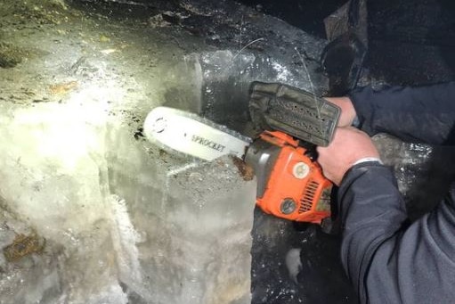 Hands are seen cutting ice with a small chainsaw