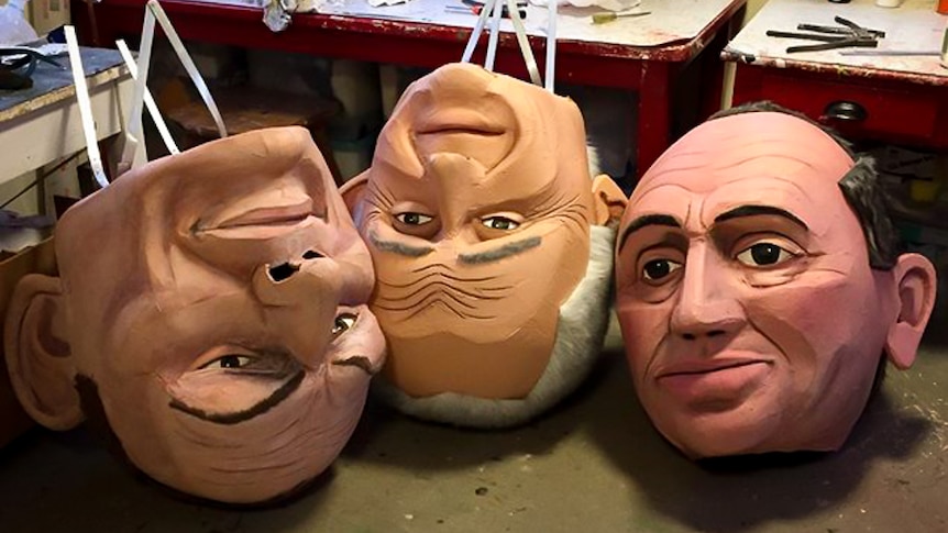Three giant puppet heads are on the floor of a workshop.