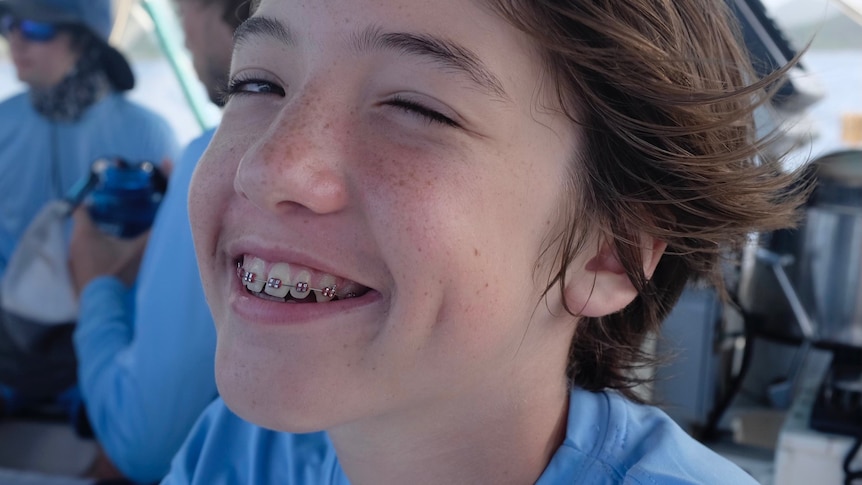 Alexander Neville smiles, he has braces and is wearing a blue t-shirt.