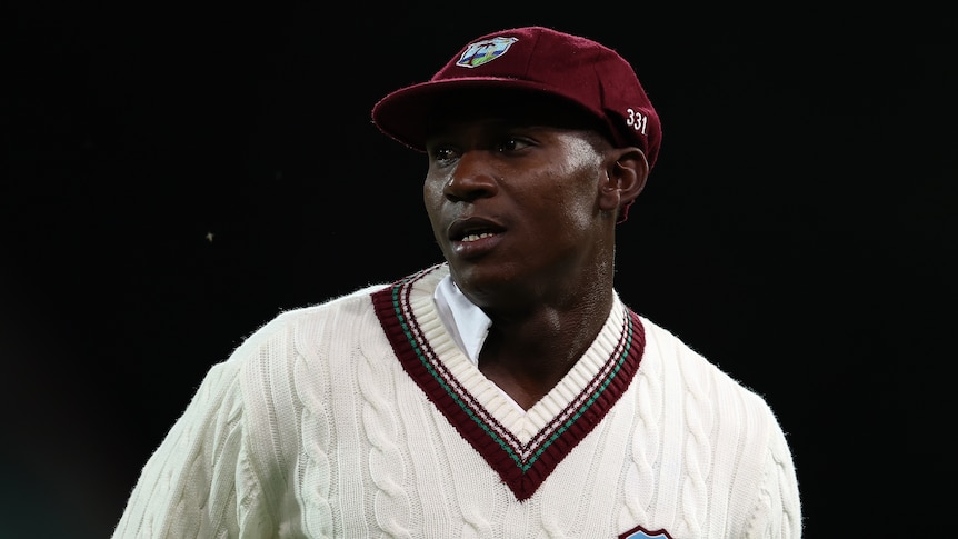 A West Indies cricketer stands wearing a maroon cap and sweater during a day-night Test match in Adelaide.