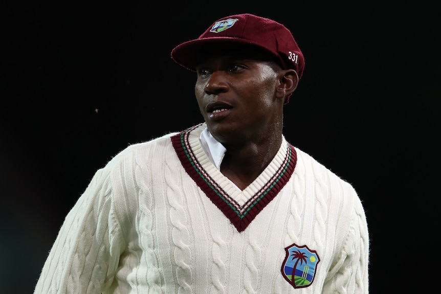 A West Indies cricketer stands wearing a maroon cap and sweater during a day-night Test match in Adelaide.