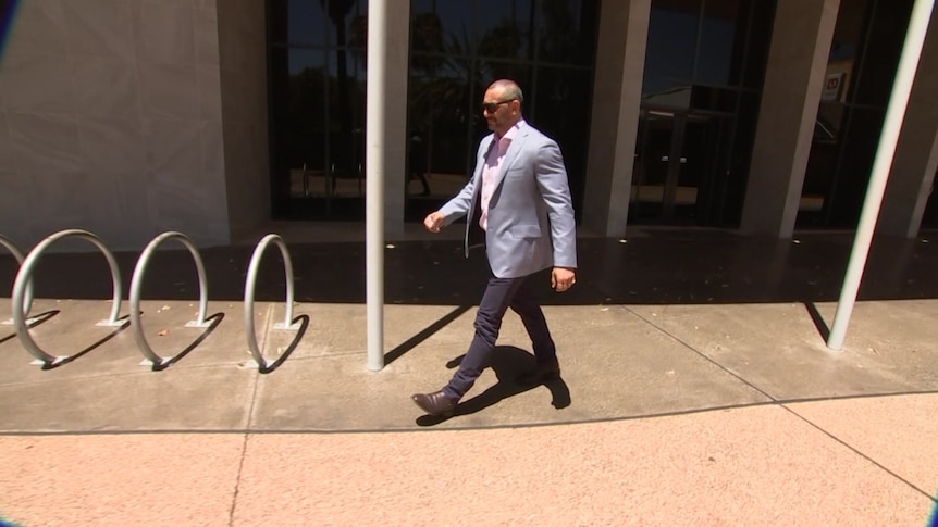 man in blue blazer and navy blue pants with black sunglasses walking on grey concrete