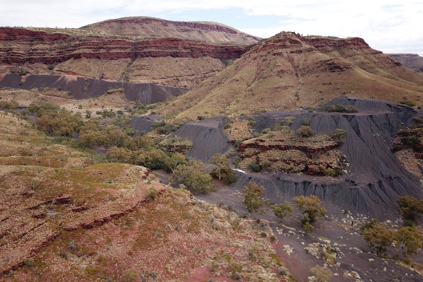 Long-distance view of dark-blue soil-like material sitting in large piles among a mountain range. 