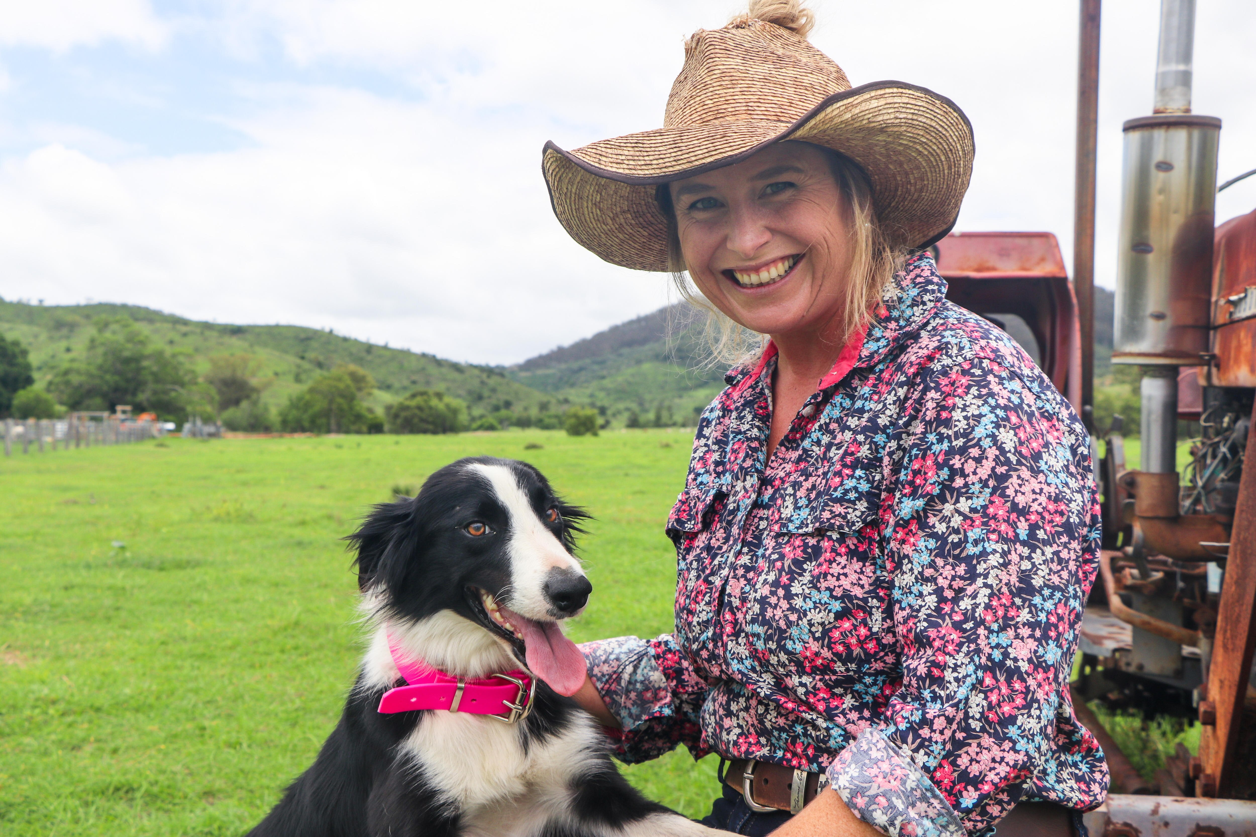 A woman sits on a rusty old tractor with a black and white cattle dog