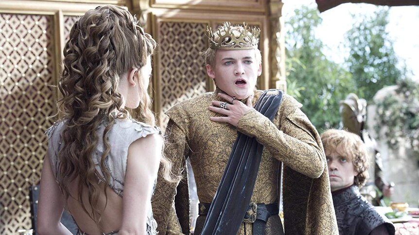Joffrey Lannister holds a hand to his throat as another one clutches a goblet. His wife stands next to him, with Tyrion behind.
