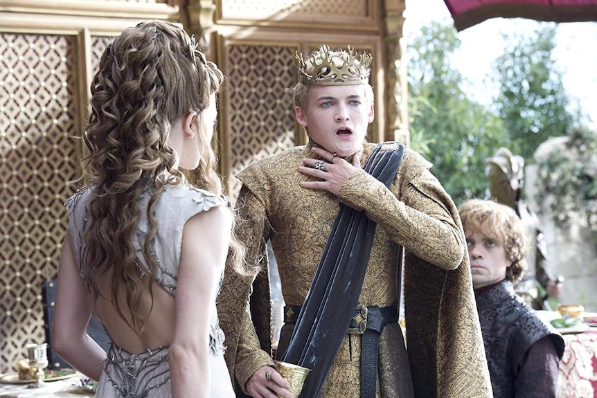 Joffrey Lannister holds a hand to his throat as another one clutches a goblet. His wife stands next to him, with Tyrion behind.