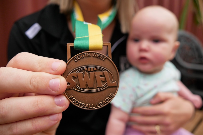 A woman holds out a medal while a baby sits in her lap