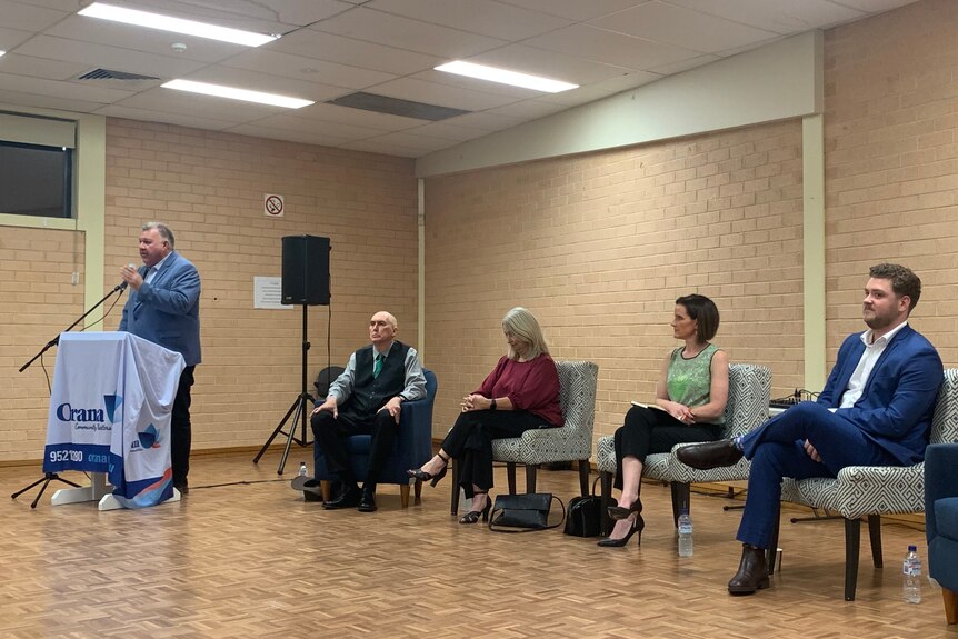 Craig Kelly speaks at a lectern while four other candidates watch on.