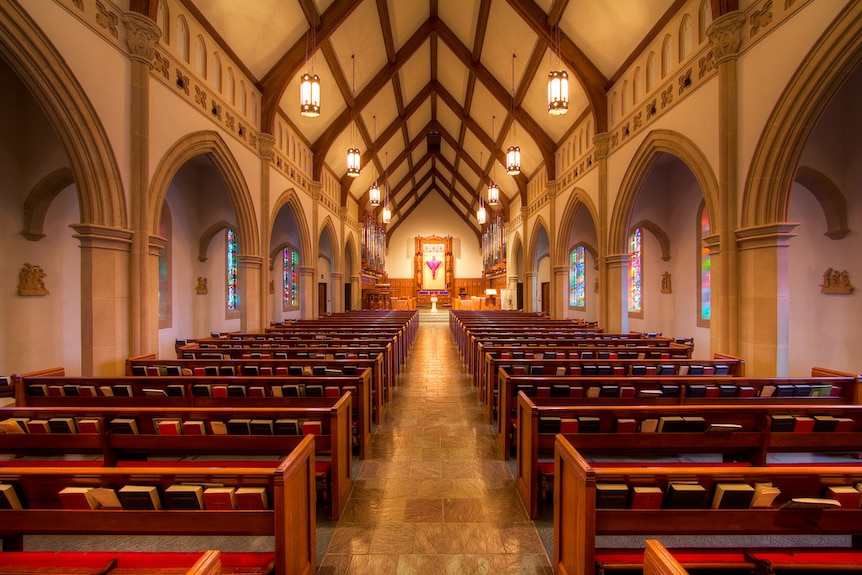 A photo from the back of a Catholic church shows pews either side of an aisle leading up to a pulpit.