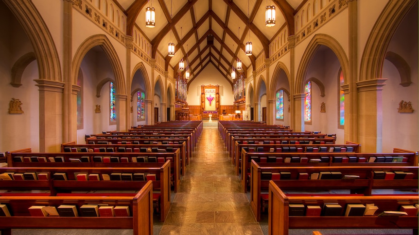 A photo from the back of a Catholic church shows pews either side of an aisle leading up to a pulpit.