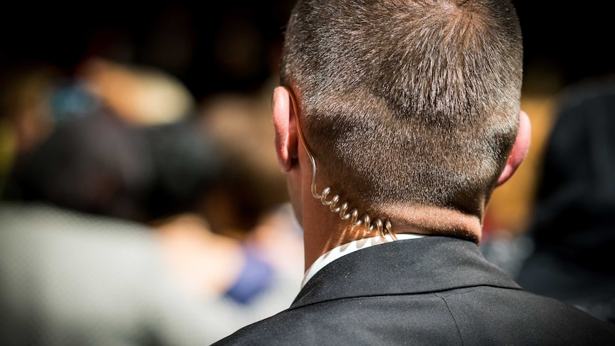 A man with short hair and in a black suit with an earpiece.