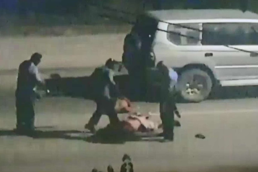 A still from a video shot across the street of three police officers kicking a man lying on the ground at night.