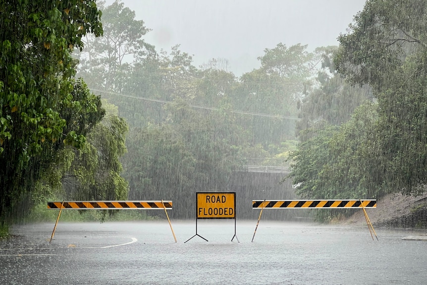 Heavy rain and road blocked with a 'road flooded' sign.