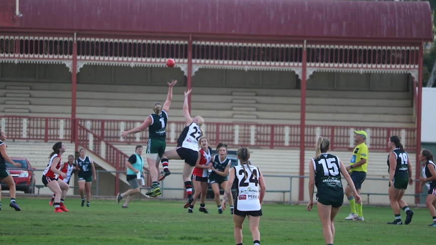 A group of women playing football, including two women from opposing team jumping up to ruck the ball