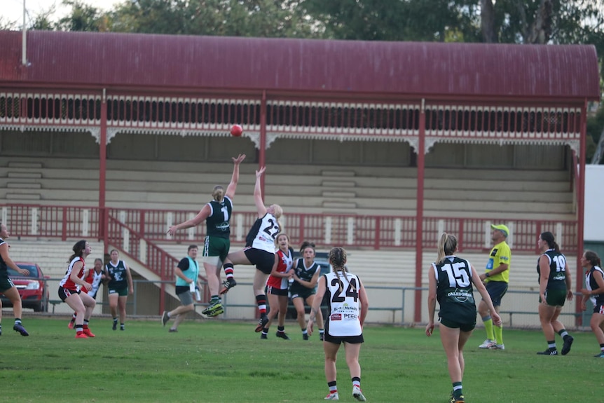 A group of women playing football, including two women from opposing team jumping up to ruck the ball