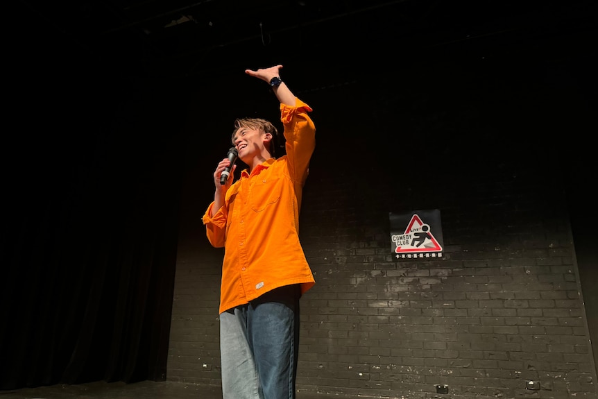 A man gestures with his hand while standing on a stage and speaking into a microphone.