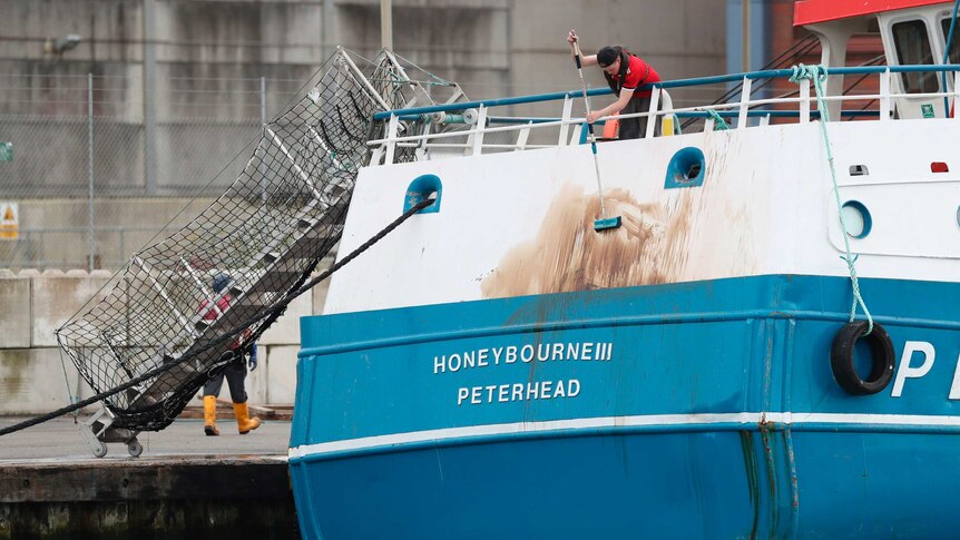 A crew member cleans marks from the stern of the Honeybourne 3, a Scottish scallop dredger, after the clash.