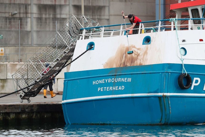 A crew member cleans marks from the stern of the Honeybourne 3, a Scottish scallop dredger, after the clash.