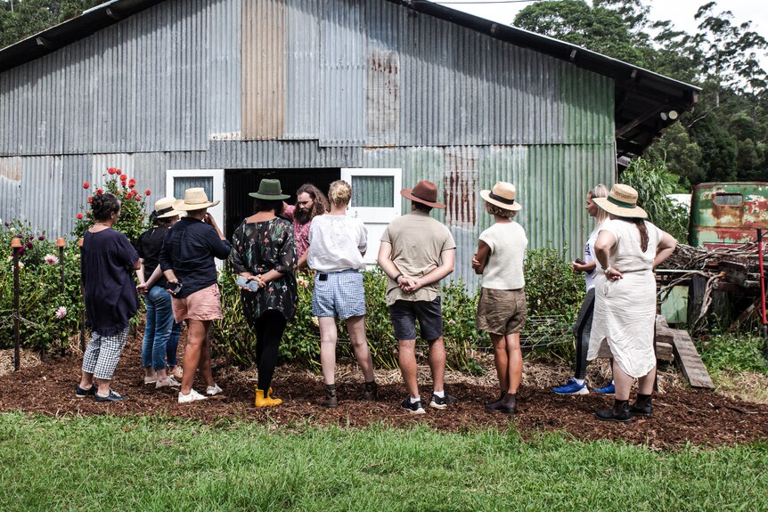 a group of people stand in front of a garden bed near a shed