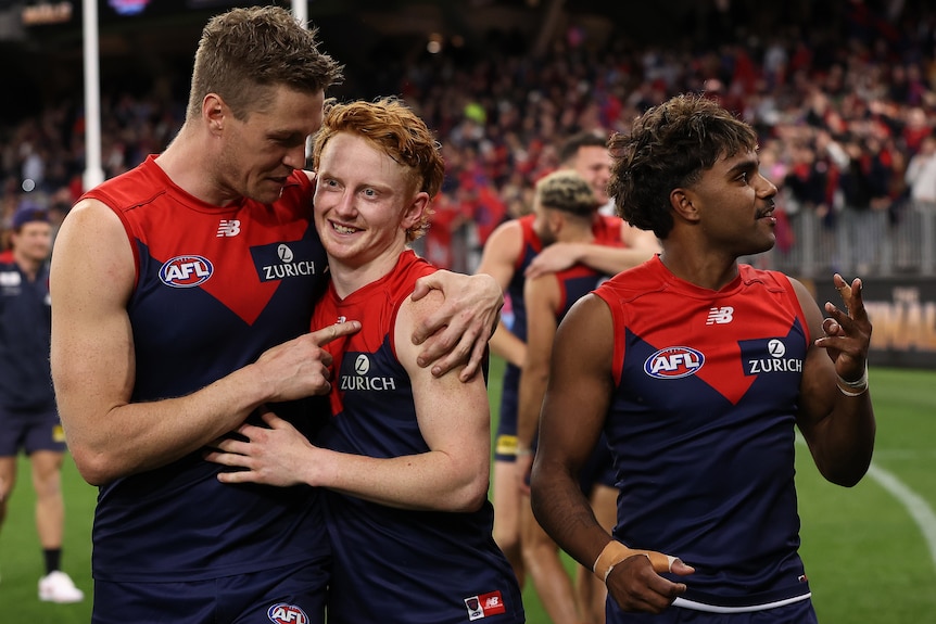 Three Melbourne Demons AFL players walk around Perth Stadium after beating Geelong.