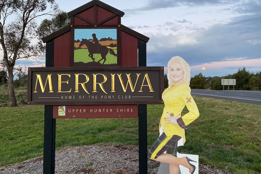 A cardboard cut-out of Dolly Parton standing next to Merriwa's town sign.