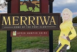 A cardboard cut-out of Dolly Parton standing next to Merriwa's town sign.