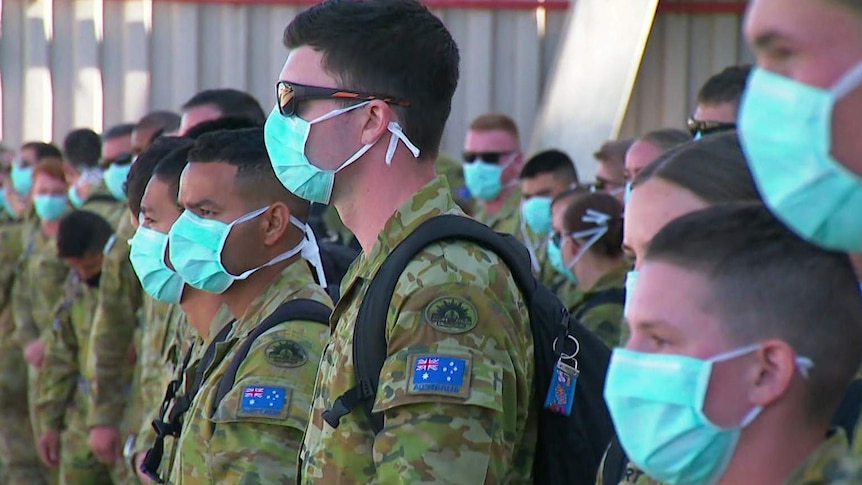 ADF officers lined up on arriving in Melbourne wearing blue surgical masks.